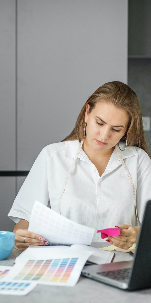 Woman sits at table in modern office next to color palette and fabric samples for design project.